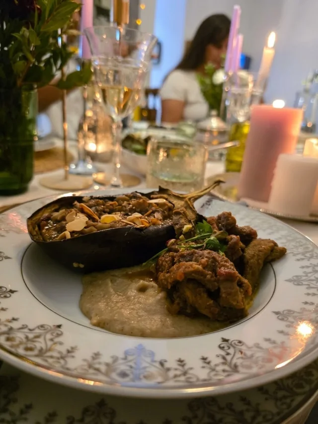 Une aubergine garnie et son accompagnement, servis dans une assiette fleurie à la lueur des bougies